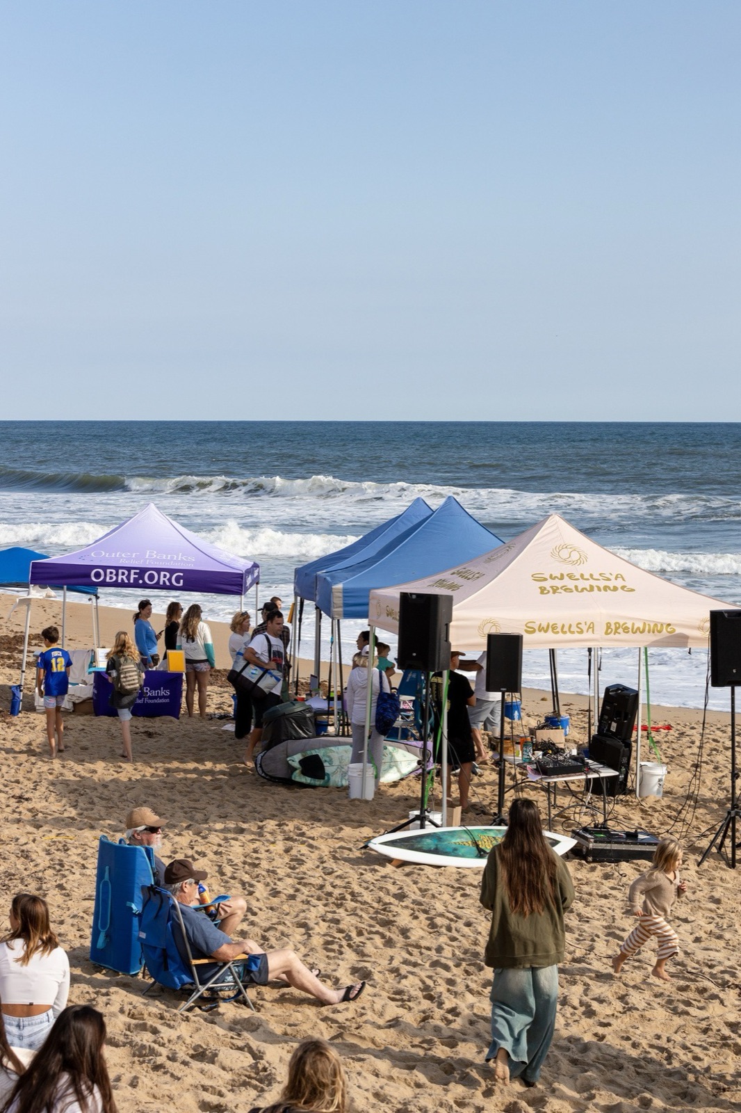 Event tents from Outer Banks Relief Foundation and Swells'a Brewing line the beach